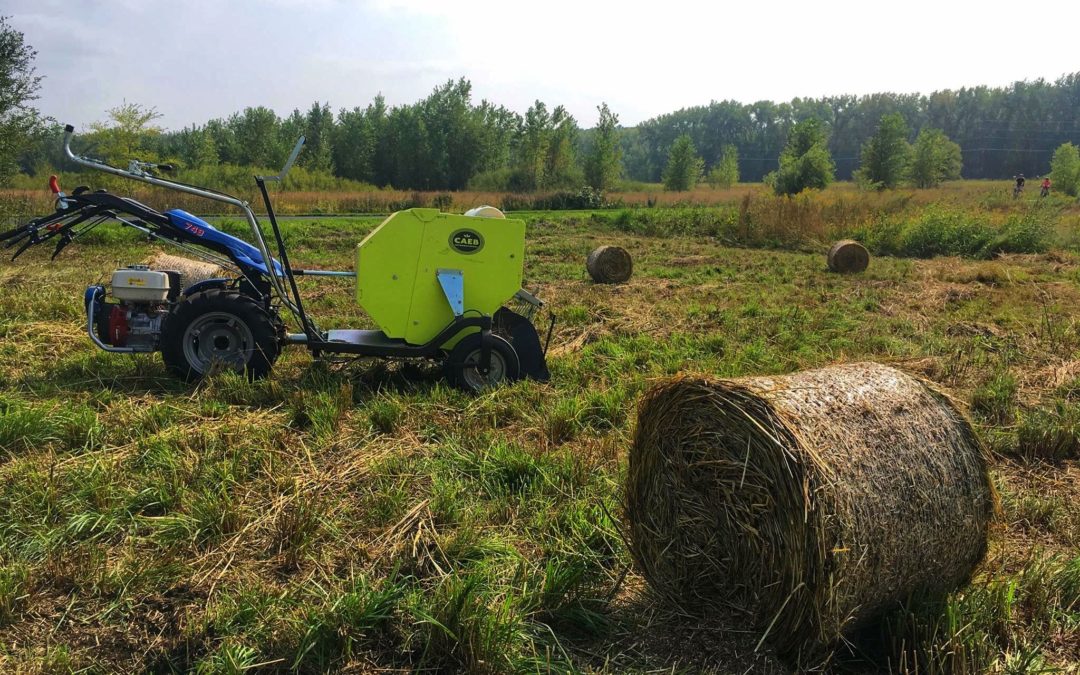 A walk behind tractor, with haying attachment, sits in a field of hay bales for blog post