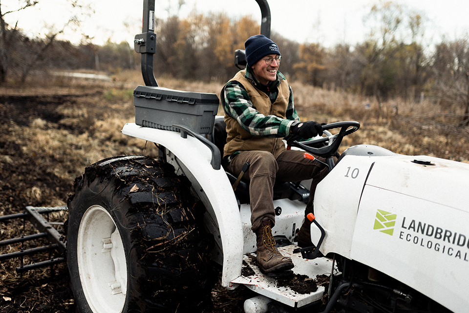 A tractor mows invasive weeds in a large flowery prairie